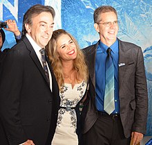 Three people smiling for a photograph before a Frozen-themed red carpet backdrop