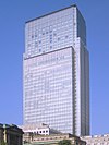 Ground-level view of a rectangular, glass high-rise; adjoining the high-rise is a stone building featuring columns