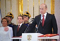 Владимир Путин произносит текст присяги на инаугурации, держа правую руку на специальном экземпляре Конституции, по левую руку расположен знак президента