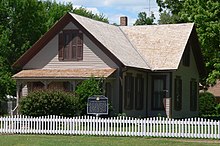 One-and-a-half-story house with gable roof and small front porch; surrounded by picket fence