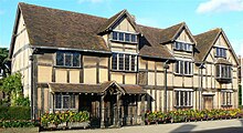 A two-story house with wattle and daub walls, a timber frame, and a steeply pitched roof.