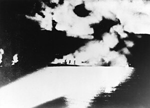 Освещённый прожекторами японских кораблей горящий тяжёлый крейсер Куинси, впоследствии затонувший в результате многочисленных попаданий снарядов и торпед японских крейсеров. Огонь слева вдали, вероятно, пожар на тяжёлом крейсере Винсенс, также получившем тяжёлые повреждения от артиллерийского огня и торпед и впоследствии также затонувшем[1].
