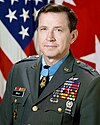 Portrait of a dark-haired white man wearing a military uniform with many ribbons, pins, and badges.