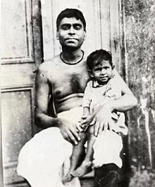 An Indian man with bare chest holding a smiling child on his lap