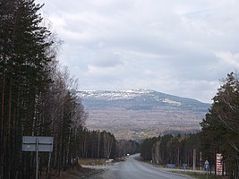 Горный участок дороги, вид в западном направлении на юго-восточный склон северо-восточной оконечности (на фото «Первая Сопка») хребта Уреньга западнее Златоуста. Перевал через хребет правее за деревьями. Пересечение с дорогой 75К-092 Златоуст — Веселовка. Ранее 2012 года