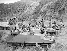 Black and white photograph of men wearing military uniforms standing on top of tanks parked on a grassed area