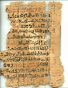 Древний, рванный и фрагментарный папирус, с рукописным почерком в черных и красных чернилах