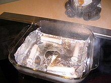 Алюминиевая фольга в квадратной посуде из пирекса с водой, с разрывом там, где фольга расплавилась