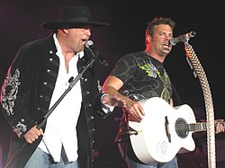 Eddie Montgomery and Troy Gentry of Montgomery Gentry singing into microphones, with Gentry also playing a white guitar