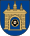 A coat of arms depicting a grey castle with three towers topped by crosses with a human head on the front door all on a blue background