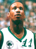 A man, wearing white shirt with a logo and the word "NBA PLAYERS" on the front, is standing and posing for a photo.