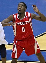 A basketball player, wearing a red jersey with the word «HOUSTON» and the number 0 on the front, stands on a basketball court.