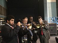 Four men in suits hold trumpets to their lips