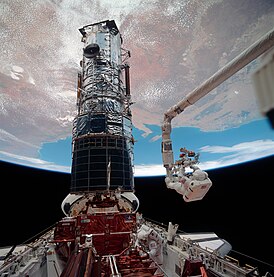 Астронавт Масгрейв поднимается на вершину Хаббла при помощи манипулятора Канадарм