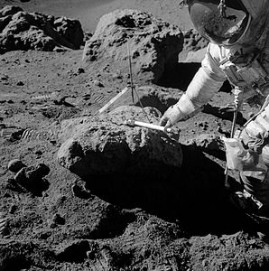 Дэвид Скотт собирает образцы лунной породы у валуна на краю борозды Хэдли (Station 9a). Фотографирующий его Джеймс Ирвин отражается в стекле гермошлема Скотта