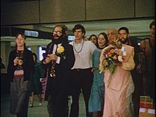 Allen Ginsberg accompanies the saffron-clad swami and a group of young followers in the airport lounge