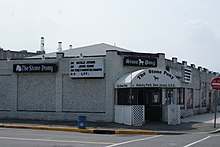 A white brick building on a city street corner. On the side of the building, and on the entrance awning is «The Stone Pony.»