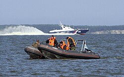 Военнослужащие пограничных органов ФСБ России задерживают лодку условных нарушителей государственной границы на учениях в районе пограничного пункта «Мамоново». На заднем плане: пограничный сторожевой катер ПСКА-306 проекта 12200 из состава ПУ ФСБ России по Калининградской области (2011 год).